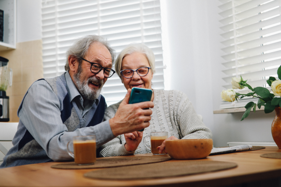 Expenses That Could Drain Your Retirement Accounts Older couple looking at a smartphone at the kitchen table, discussing retirement accounts